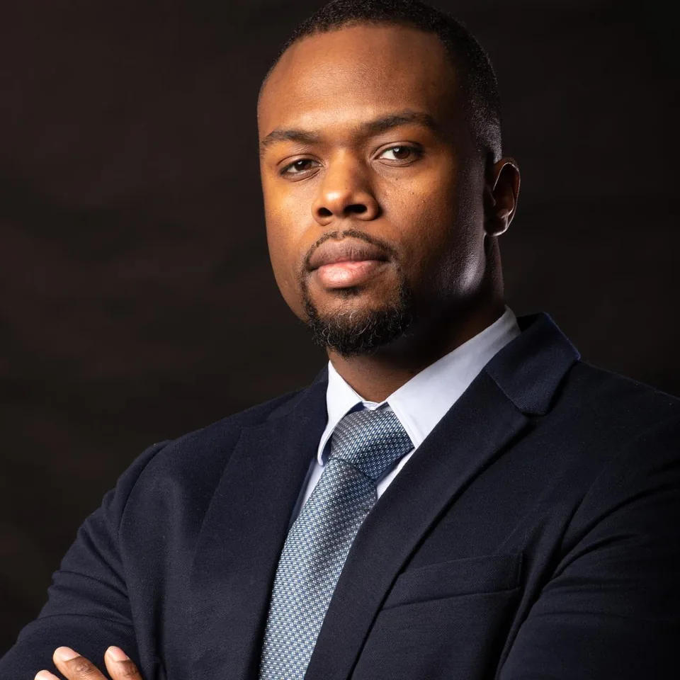 David Mwaku, studio portrait, navy suit, arms crossed.