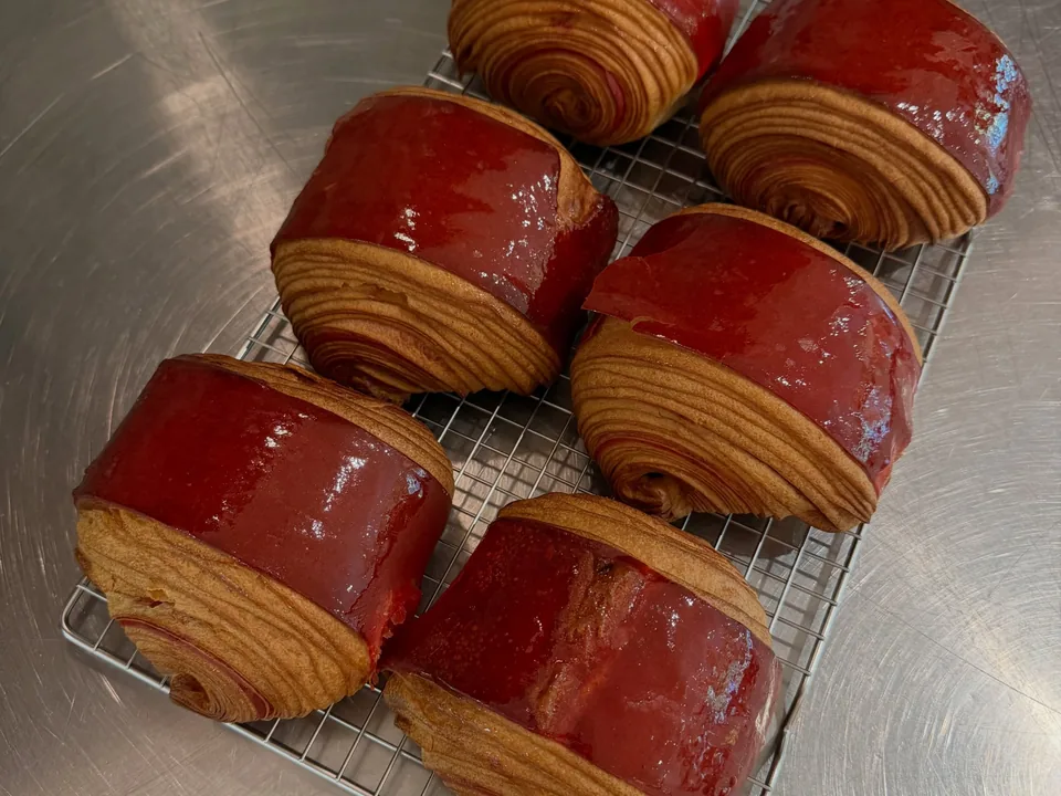 Des couques chocolat-framboise au feuilletage bien visible, nappées de rouge, sur une grille posée sur l’inox.