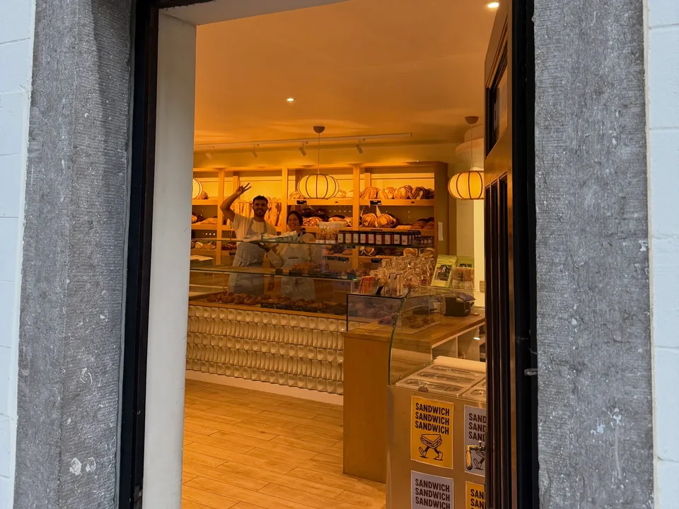 La porte ouverte de la boutique de Lasne dans son encadrement de pierre bleue : au fond, les étagères de pains et les suspensions en papier sous une lumière chaude.