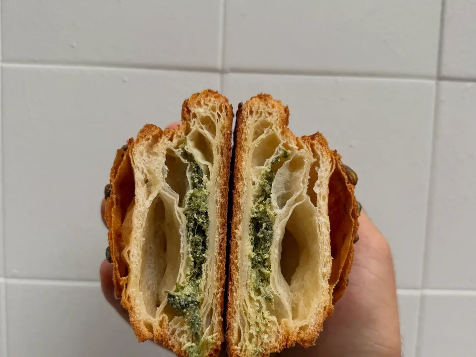 Une viennoiserie salée coupée en deux, épinards et ricotta au cœur d’un feuilletage alvéolé, tenue à la main.