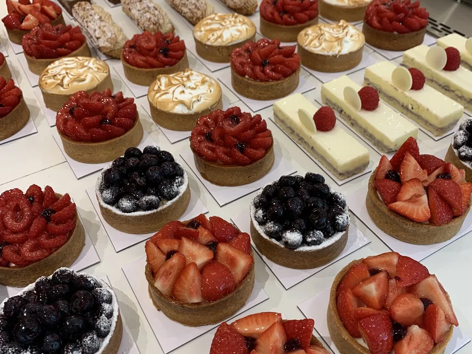 La vitrine des pâtisseries individuelles en rangs : tartelettes aux fraises, aux myrtilles et au citron meringué, entremets à la framboise, éclairs.
