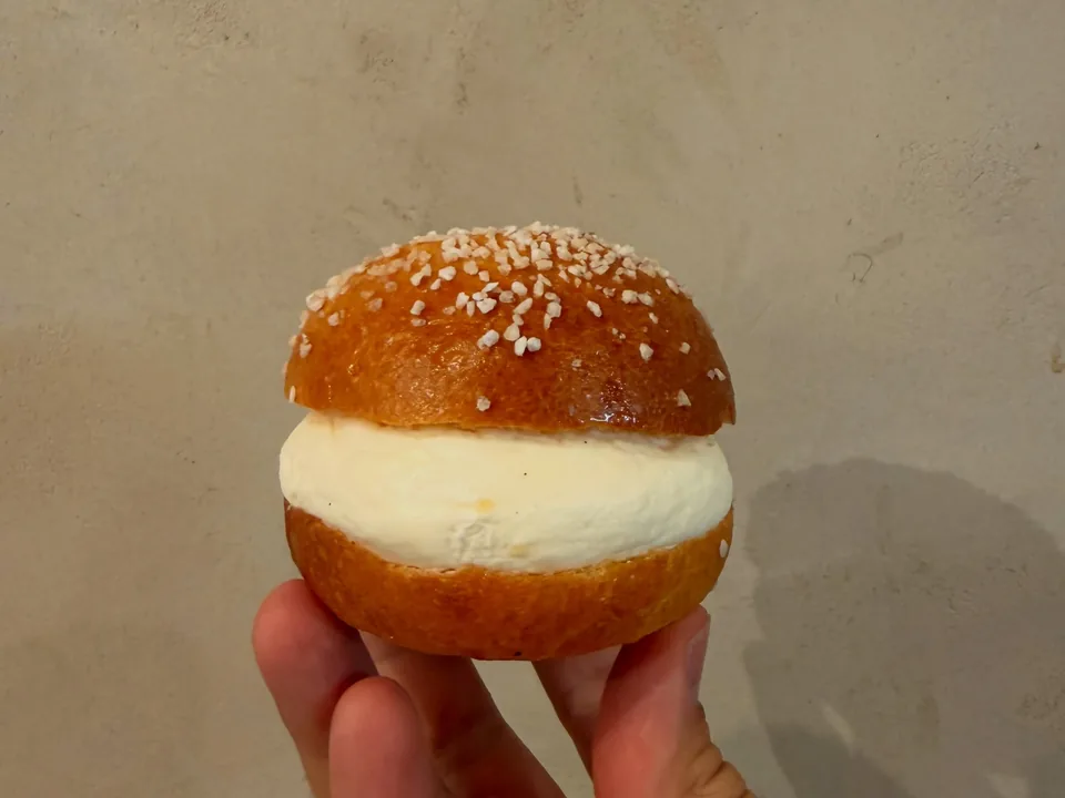 Une mini tropézienne, brioche au sucre perlé garnie de crème, tenue à la main.