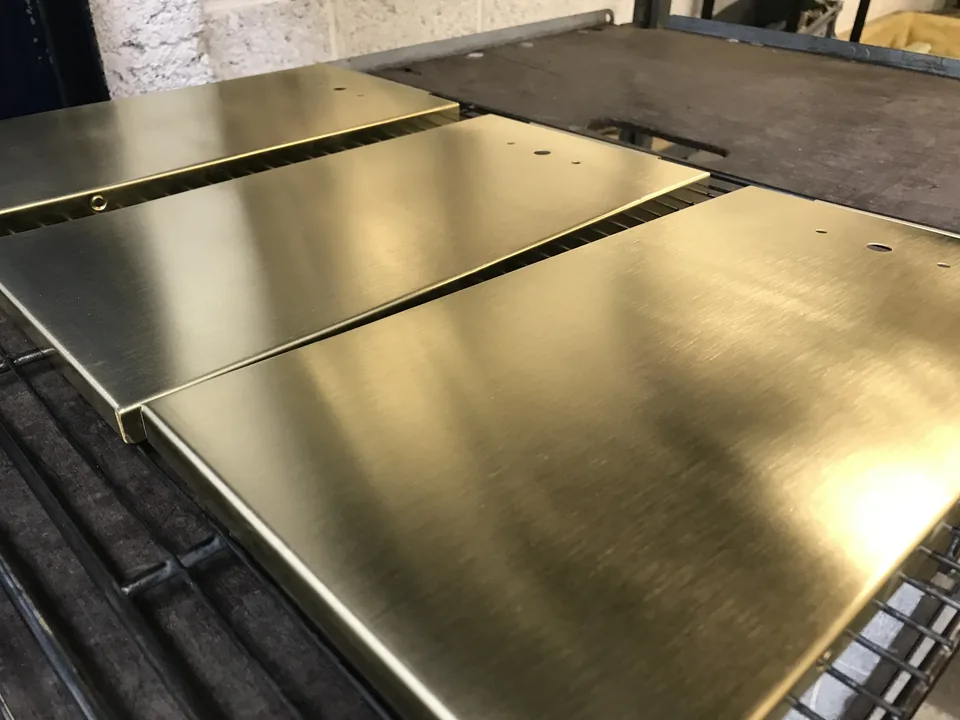Three brushed golden brass panels on drying racks, light running along the brushed grain.