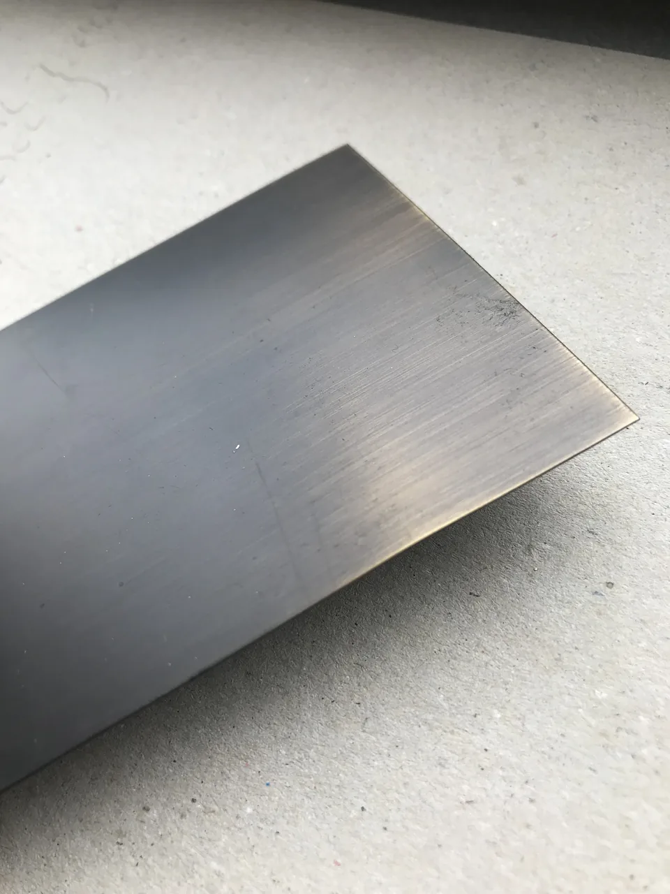 Une tôle de laiton brossé à la patine bronze sombre, reflets dorés sur les bords, posée sur du béton.
