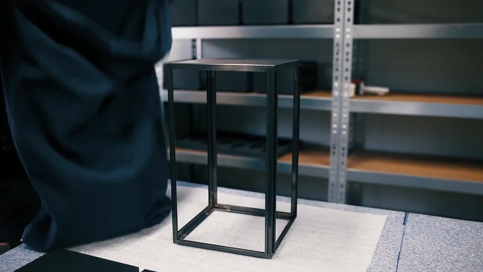 The finished black table on the packing bench, in front of metal shelving.