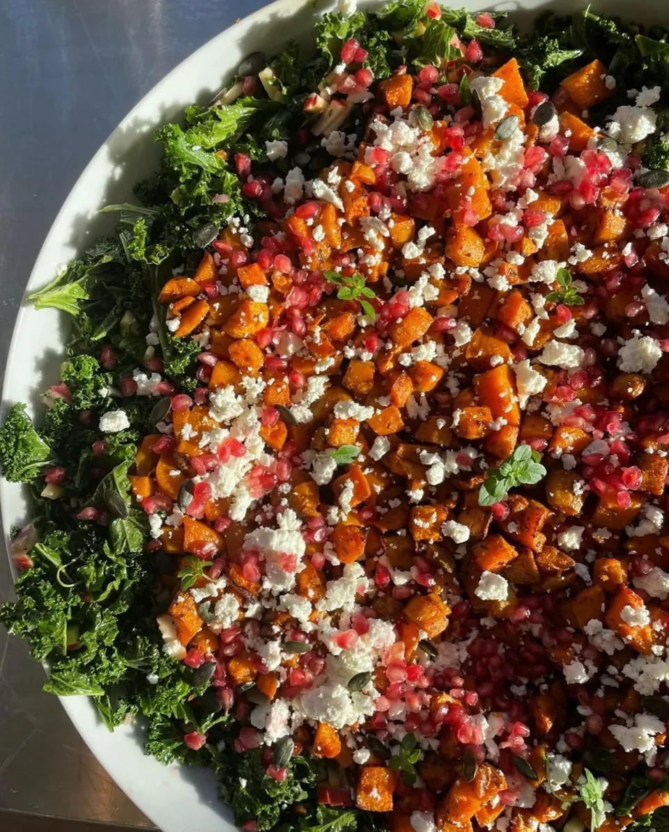 Un grand plat de courge rôtie en dés, feta, grenade et chou kale, vu de dessus.