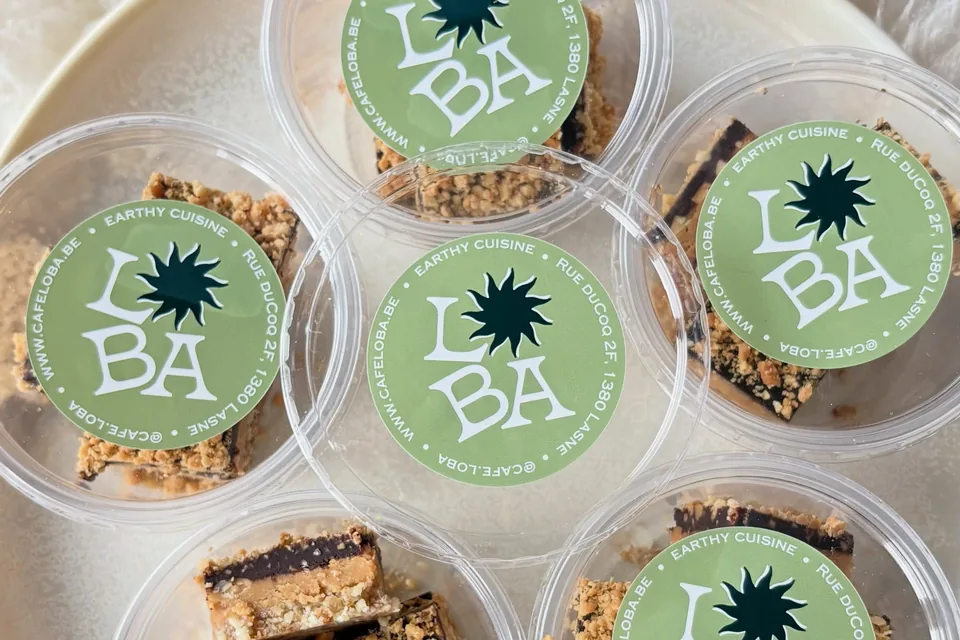 Les « Snickers » maison de Café Loba en barres, dans des pots transparents fermés par l’étiquette verte au logo Loba « Earthy cuisine », sur un plateau crème posé sur une peau de mouton.