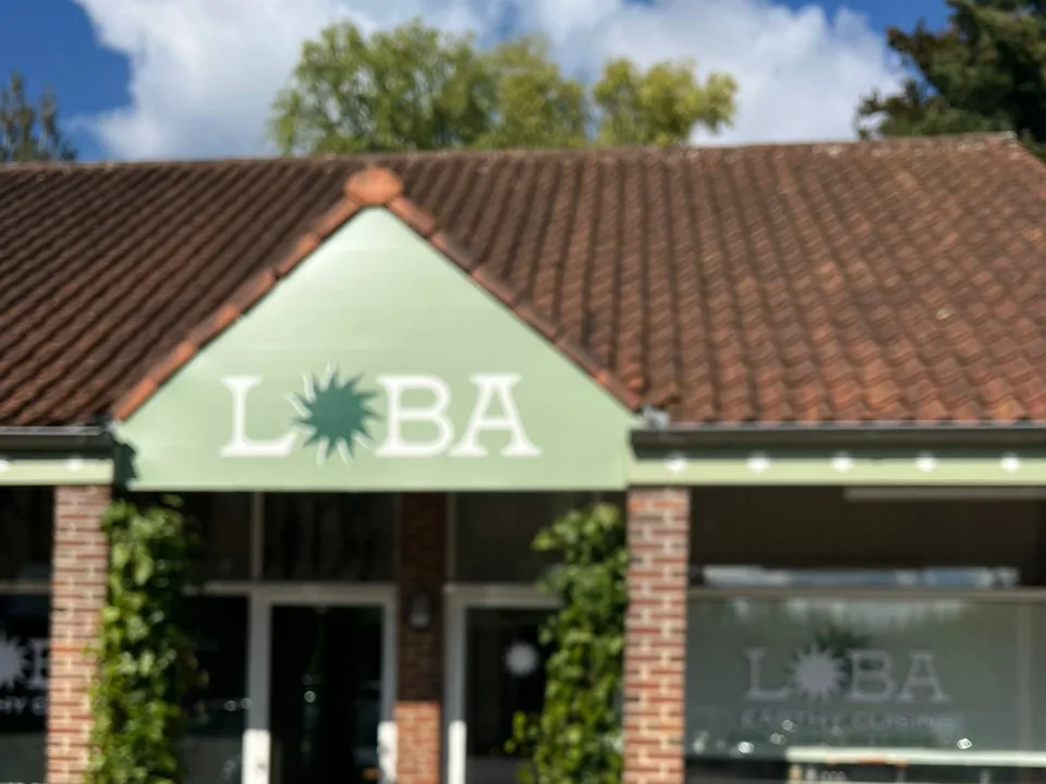 La devanture de Café Loba, rue du Coq à Lasne : un pignon vert sauge au nom de LOBA sous un toit de tuiles, des piliers de briques couverts de lierre et des vitrines au logo.