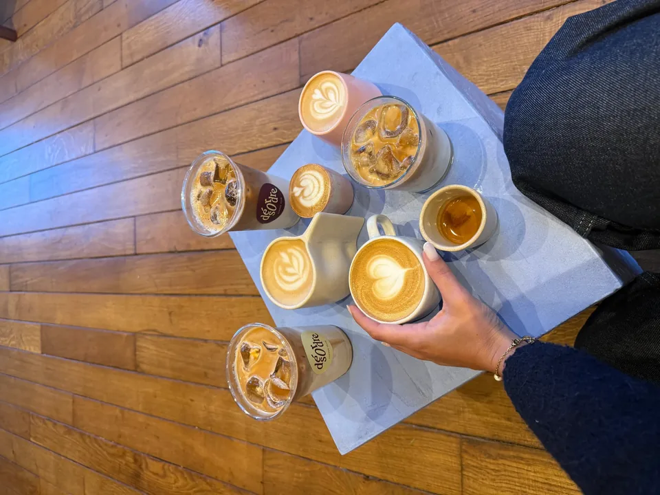 Vu d’en haut, un plateau de cafés chauds et glacés aux gobelets Désordre, tenu au-dessus du parquet.