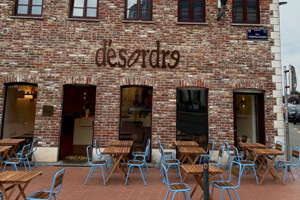 The front of Désordre, a red-brick house with the café’s name in metal letters, its terrace of wooden tables and blue chairs on the pavement.