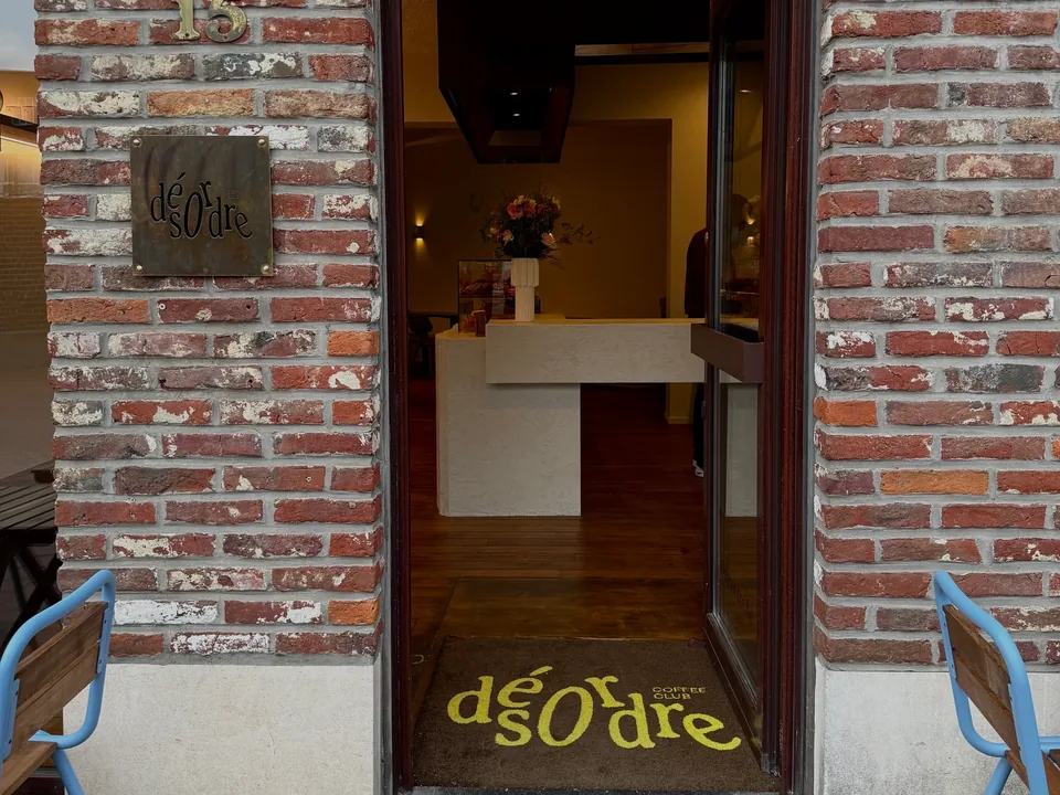 The open door of number 15 in the brick wall: a square sign, a yellow doormat with Désordre’s name and, at the back, the counter with flowers.