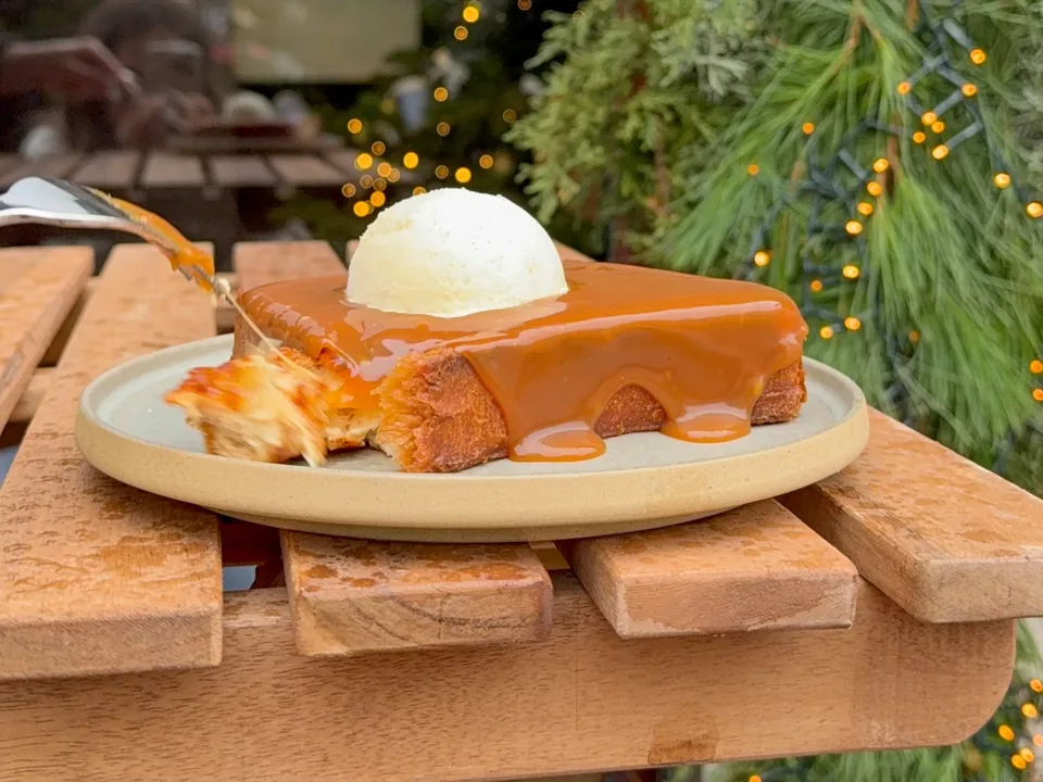 Un pain perdu nappé de caramel et une boule de glace vanille, sur une table de terrasse décorée de sapin et de guirlandes lumineuses.