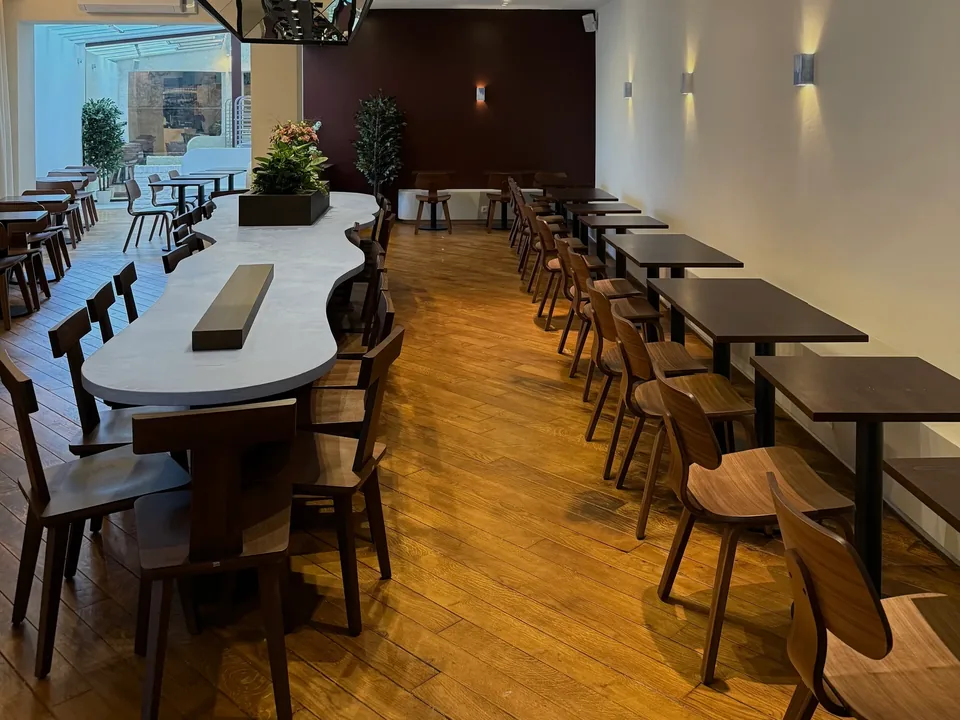The long room: a large white table with wavy edges, dark wooden chairs, a blue wave-shaped ceiling light, and the glass roof at the back.