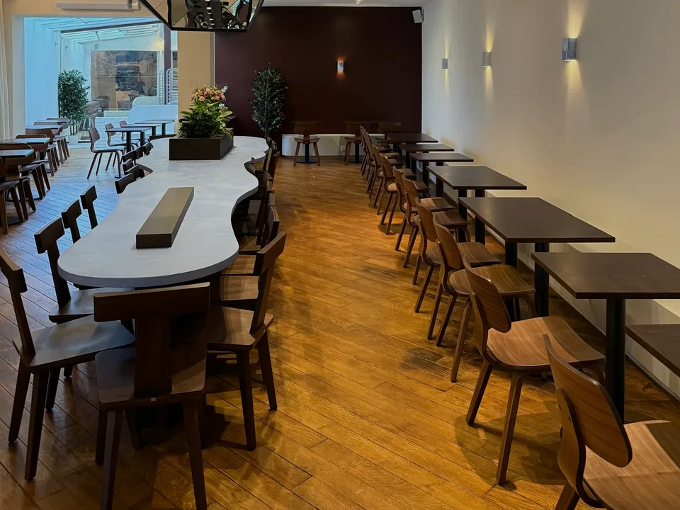 The long room: a large white table with wavy edges, dark wooden chairs, a blue wave-shaped ceiling light, and the glass roof at the back.