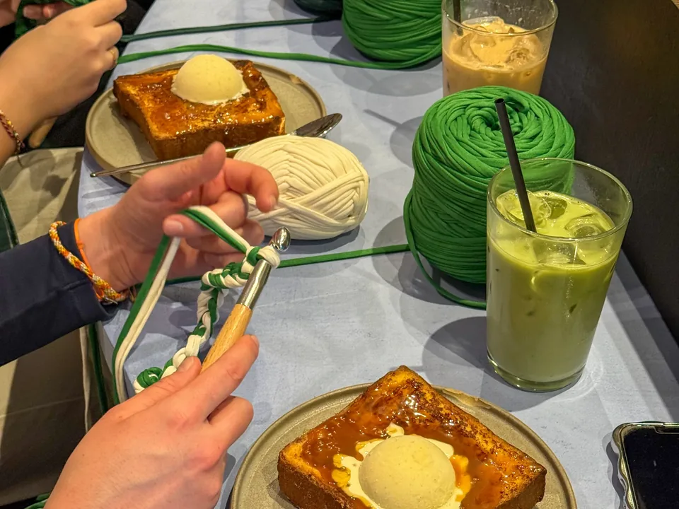 Une tablée autour de pelotes de laine vertes et blanches : des mains au crochet, des pains perdus glacés et des matchas.