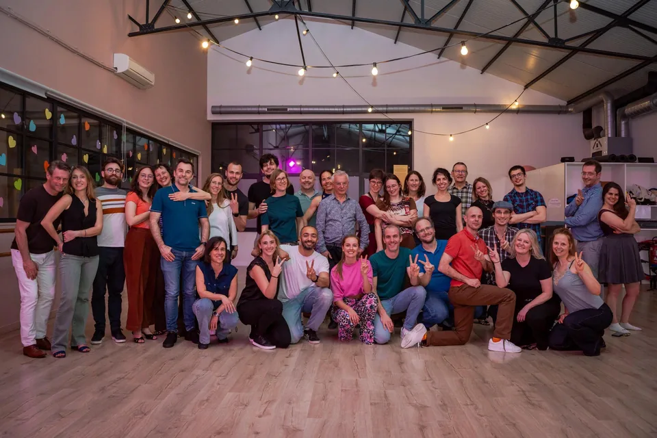 A Funnyrockers classroom: some forty dancers pose on the pale wooden floor, under a steel roof frame and a string of light bulbs, coloured hearts stuck on the windows.
