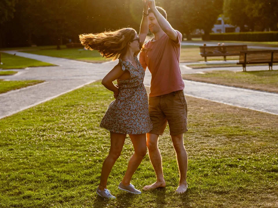 Backlit in a park, a couple dances barefoot on the grass, the dancer’s hair flying in the evening light.