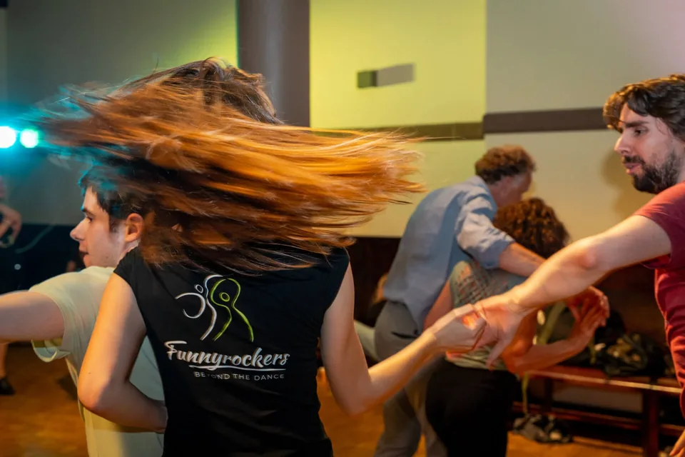 A dancer in a « Funnyrockers — Beyond the dance » T-shirt spins so fast her hair flies out, her hand in her partner’s.