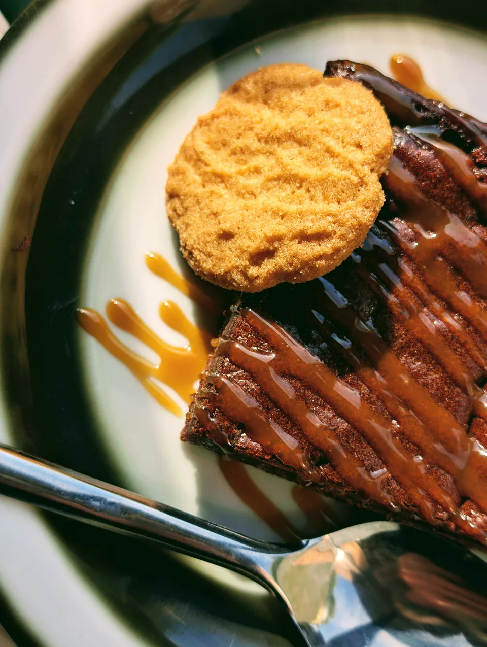 Un brownie nappé de caramel et un biscuit sur une assiette du Club House, au soleil.