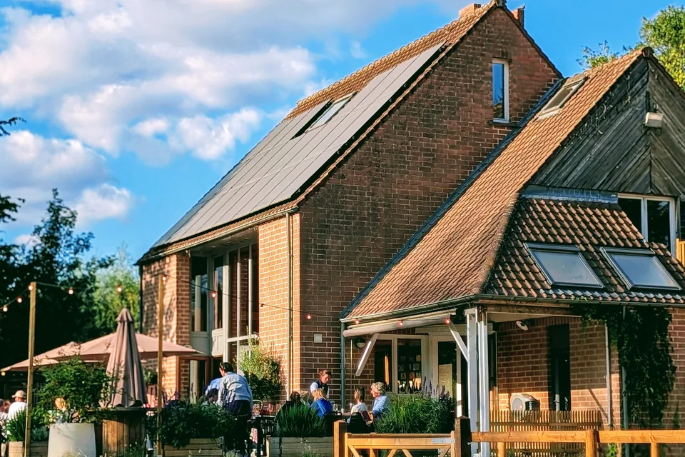The brick Club House at Glabais Hills, its terrace under parasols and string lights, seen from an arena in the late-afternoon light.