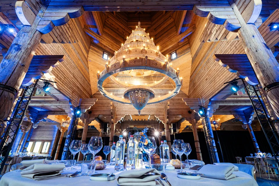 A carved-wood hall set for a gala dinner, under a large chandelier.