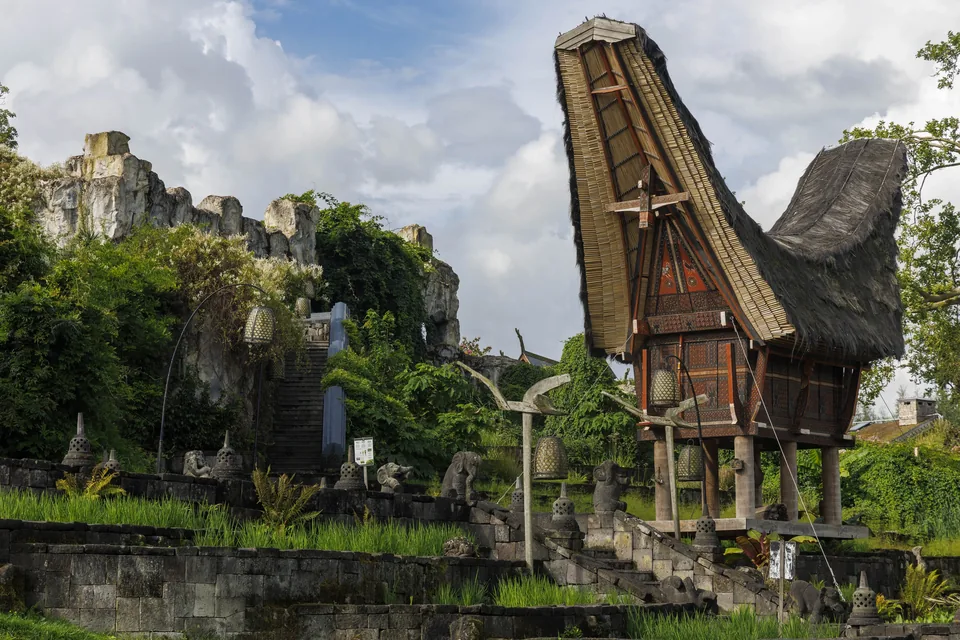 A traditional Tana Toraja house with a boat-shaped roof above stone terraces, in the Kingdom of Ganesha.