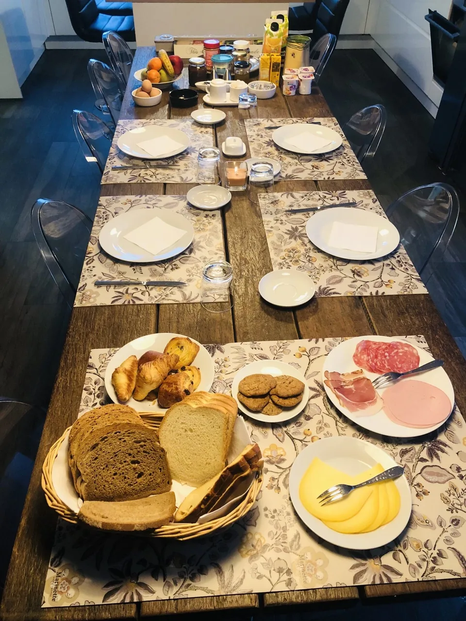 A breakfast table: bread, pastries, cold meats, cheese and jams.