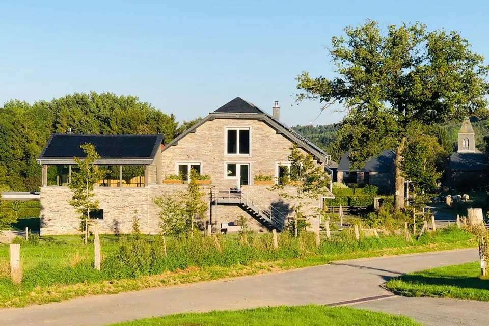 The Pegasus B&B stone house in Regné, its glazed terrace and outdoor staircase, by a lane; a large oak and the village church tower on the right.