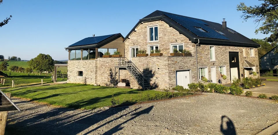 The house from the west at the end of the day: stone façade, steel outdoor staircase, glazed terrace and lawn.