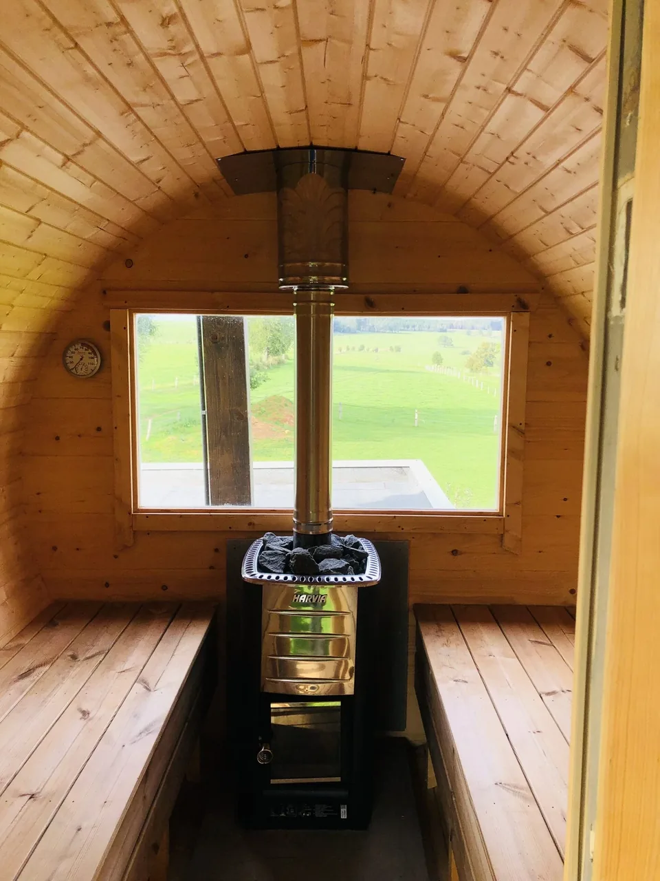 Inside the barrel sauna: wooden benches, the stove in the middle, a window onto the meadows.