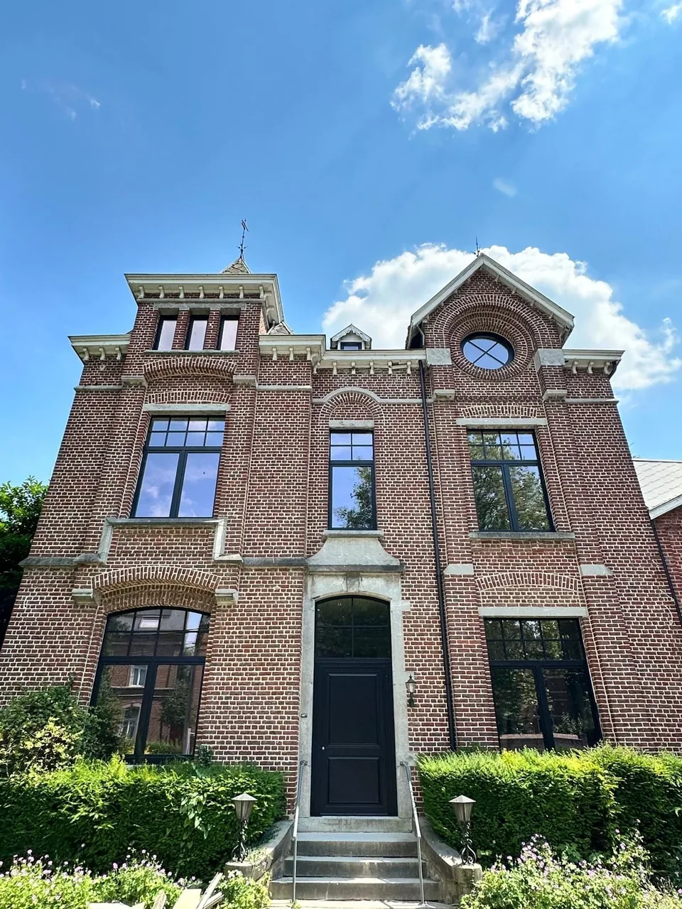The Ellie project: the red-brick façade of a nineteenth-century mansion, its new black windows with glazing bars, a round window and the black front door, under a blue sky.